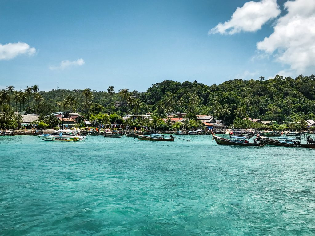 Boats lining the teal waters on the edge of a Thailand island