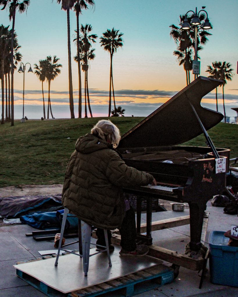 homeless man playing the piano by sunset