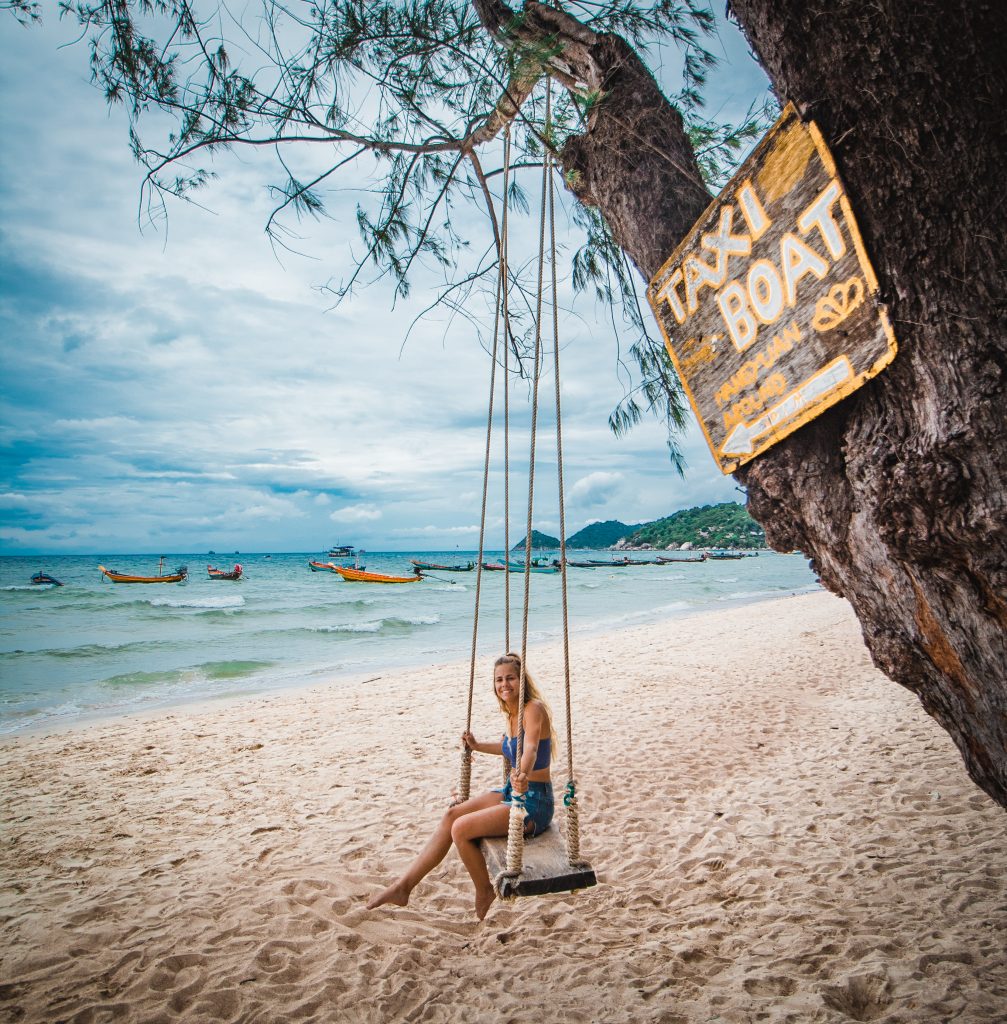 Me on a swing in Koh Tao with the taxi boat sign overlooking the water