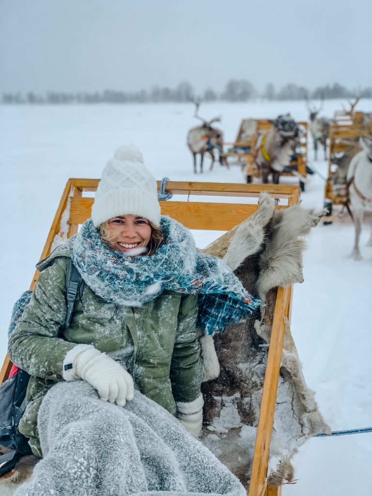 Me on the reindeer sled with reindeer in the background and snow falling